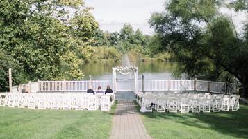 A lakeside outdoor wedding ceremony with white chairs arranged in rows, a white archway, and a wooden deck.