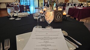Une table dressée pour le dîner de la Saint-Valentin, avec un menu indiquant des plats tels que des coquilles Saint-Jacques de Douvres et des cakes au crabe.