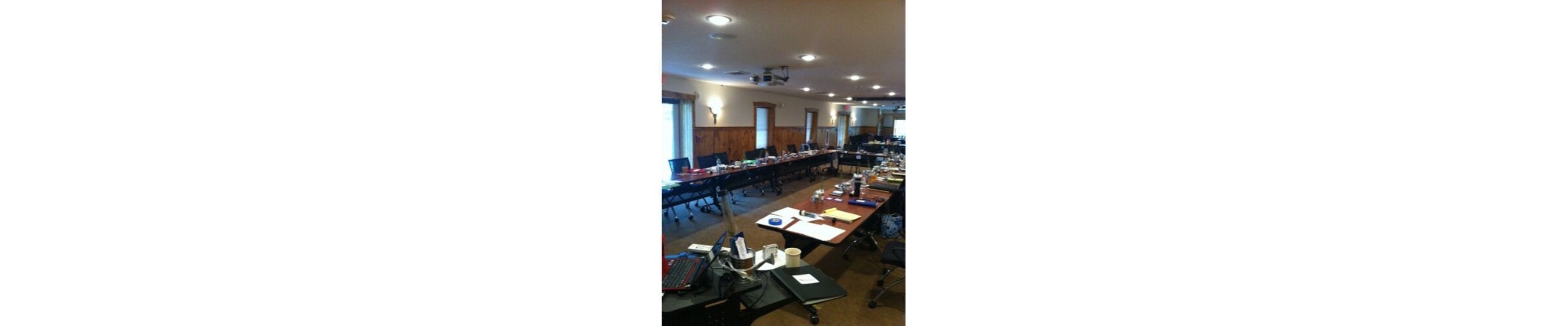 A conference room with long tables, chairs, and a projector screen.