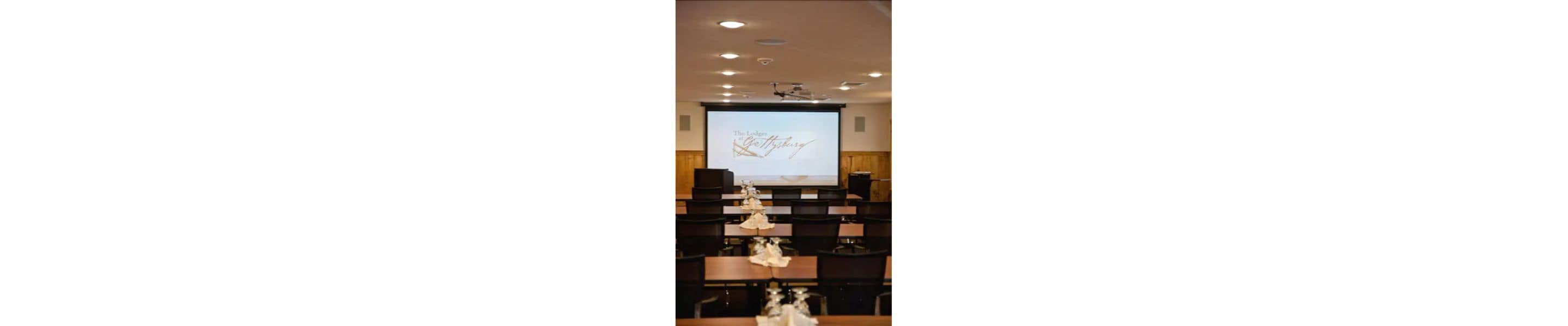 A conference room with a projection screen displaying 'The Lodge of Getting Married'.