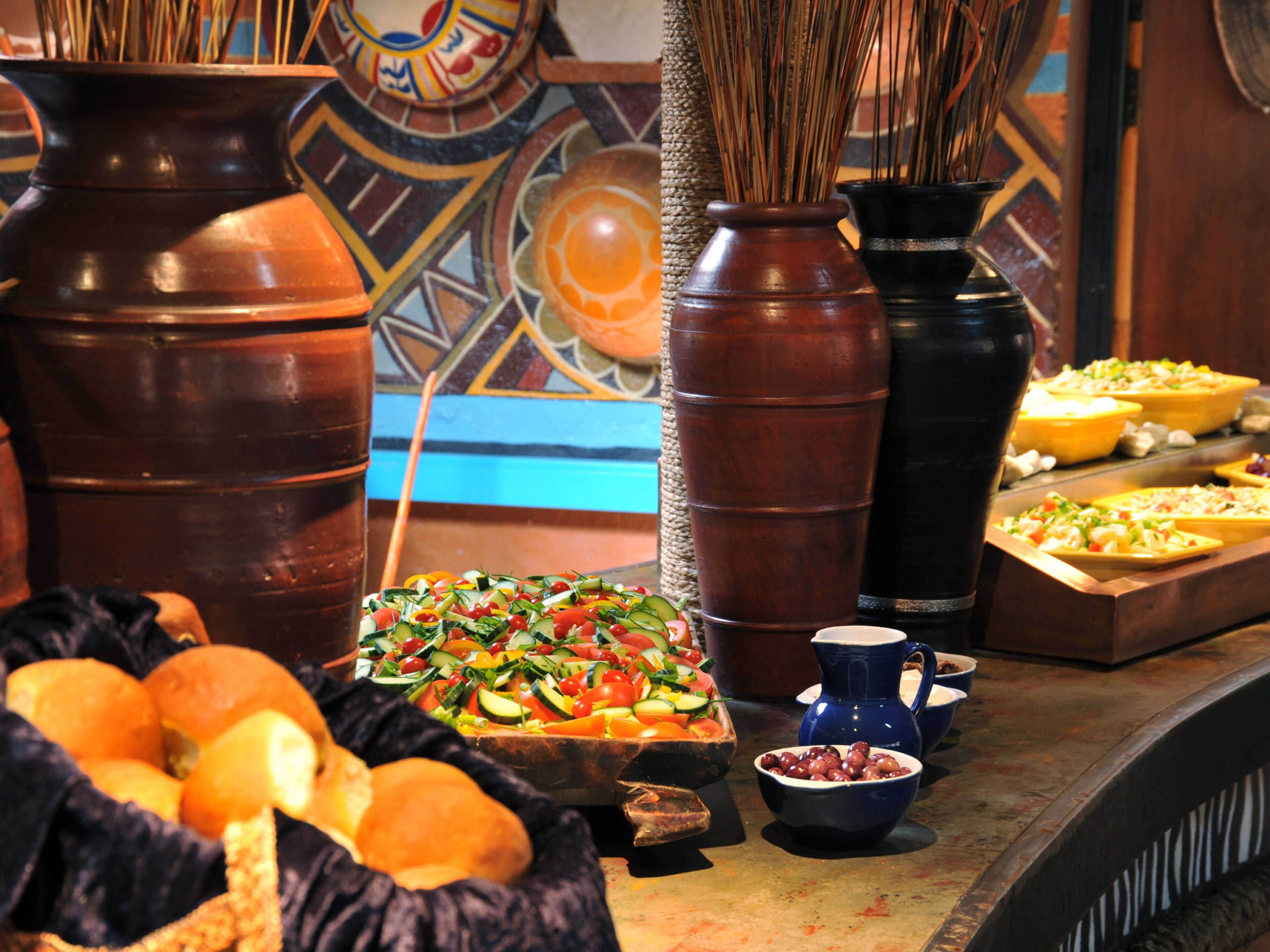 A buffet table with various food items, including a salad, bread, and bowls of olives.