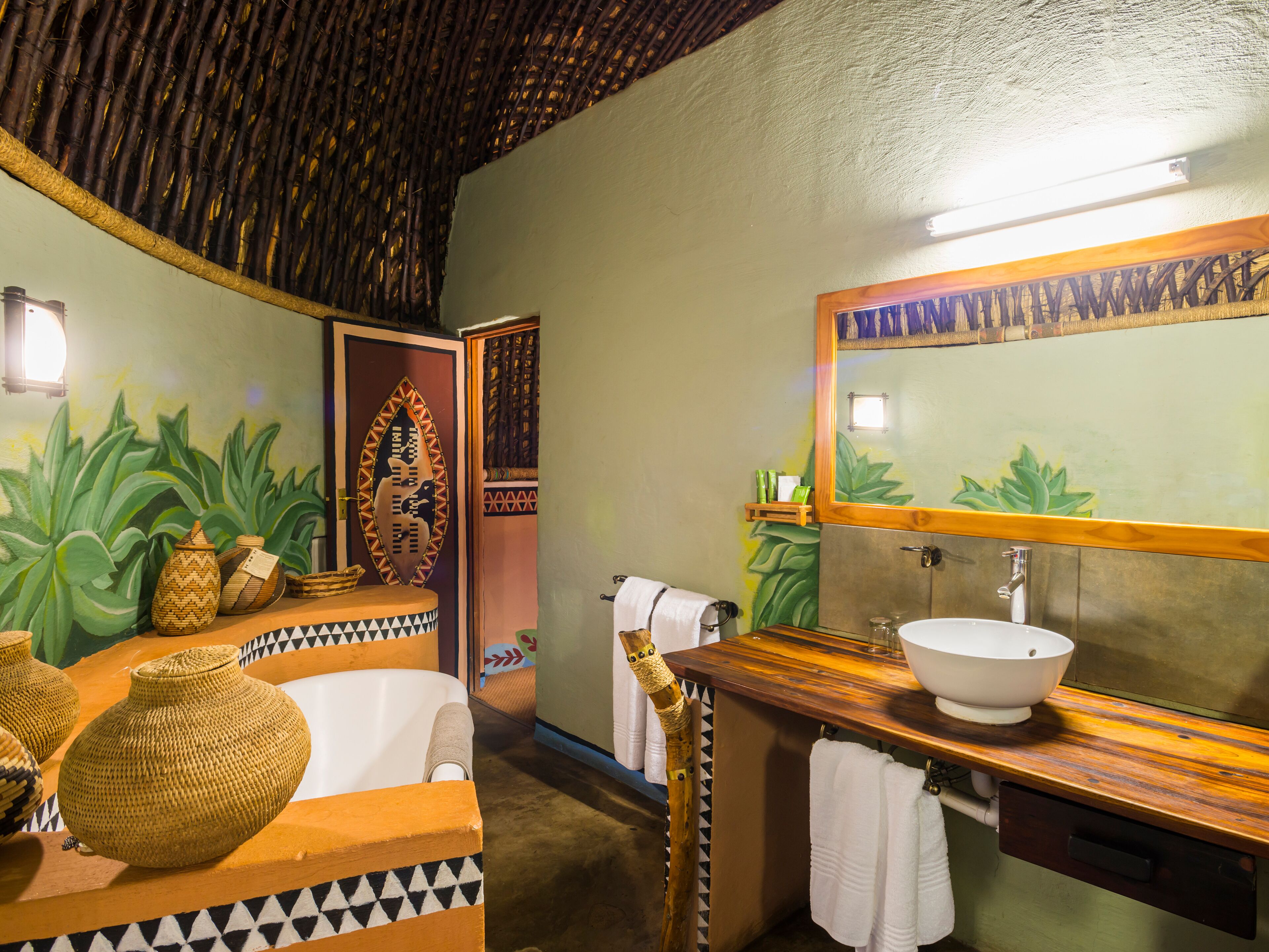 Un baño con un espejo grande, un lavabo y una bañera. Hay objetos decorativos en el mostrador y un perchero para toallas.