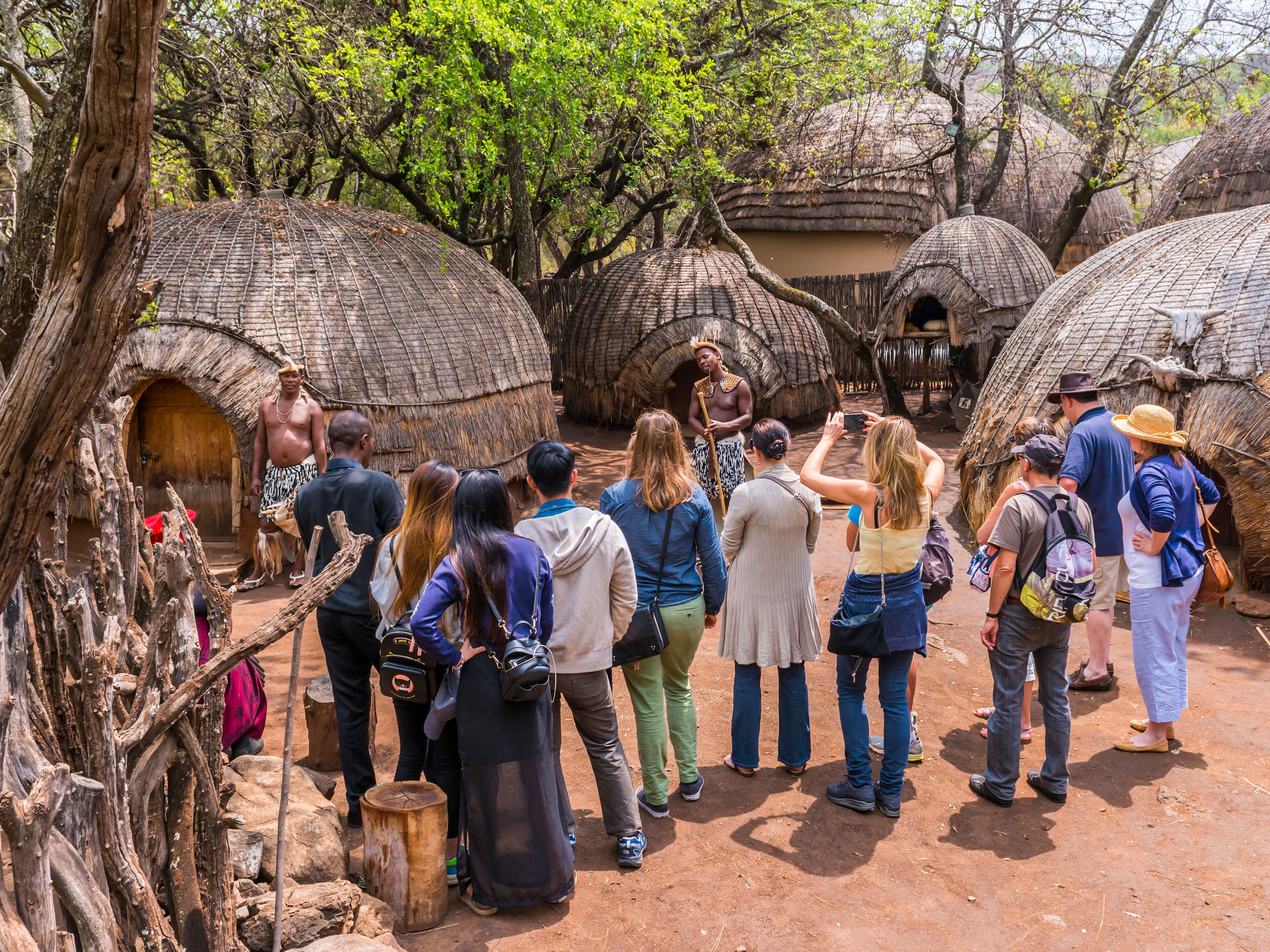 A group of tourists observing traditional huts with thatched roofs in a natural setting.