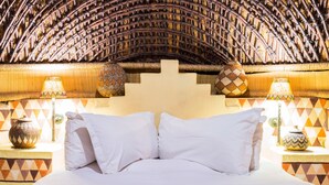 Un lit avec du linge de lit blanc, un tapis à motifs et une structure décorative tissée au plafond.
