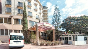 A multi-story building with a covered entrance, a van parked in front, and a tree with orange flowers to the right. - Beer Garden Inn (Addis Ababa)