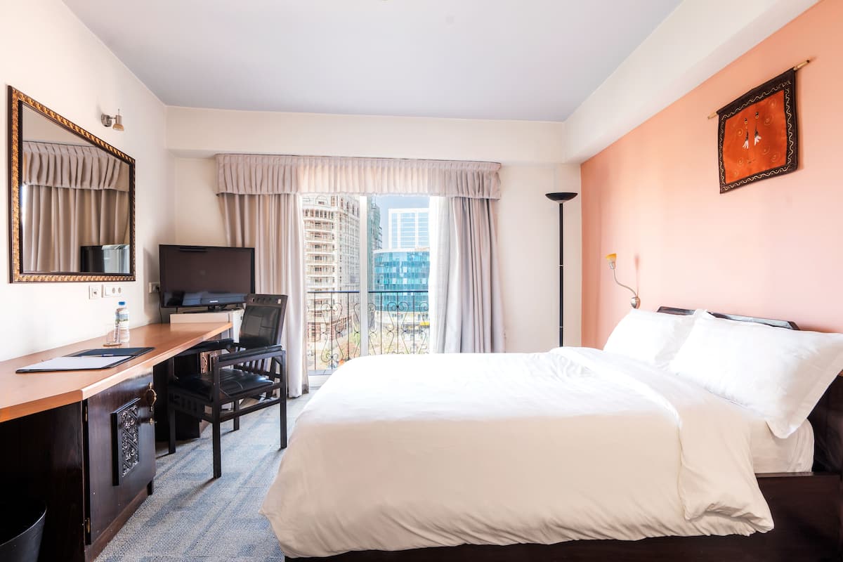 A hotel room with a bed, desk, chair, TV, and a balcony with curtains.