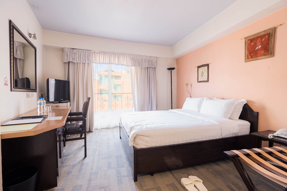 A hotel room with a bed, desk, chair, and a TV.