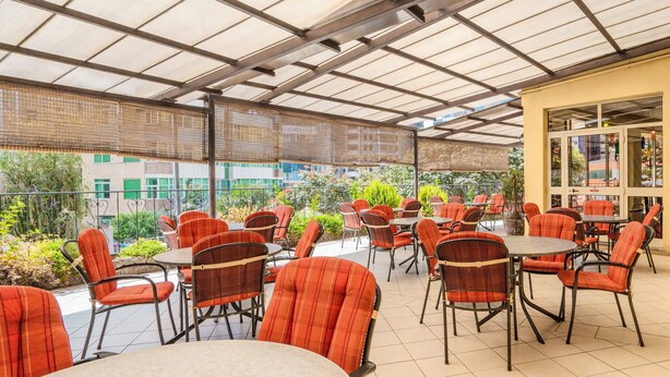 An outdoor patio area with tables and chairs, covered by a translucent roof, and surrounded by greenery. - Beer Garden Inn (Addis Ababa)