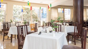 A restaurant with multiple tables set for dining, large windows with curtains, and hanging colorful lights. - Beer Garden Inn (Addis Ababa)