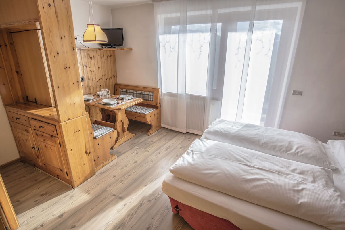 Une chambre à coucher avec un lit, un bureau en bois, une chaise et un téléviseur posé sur une étagère.