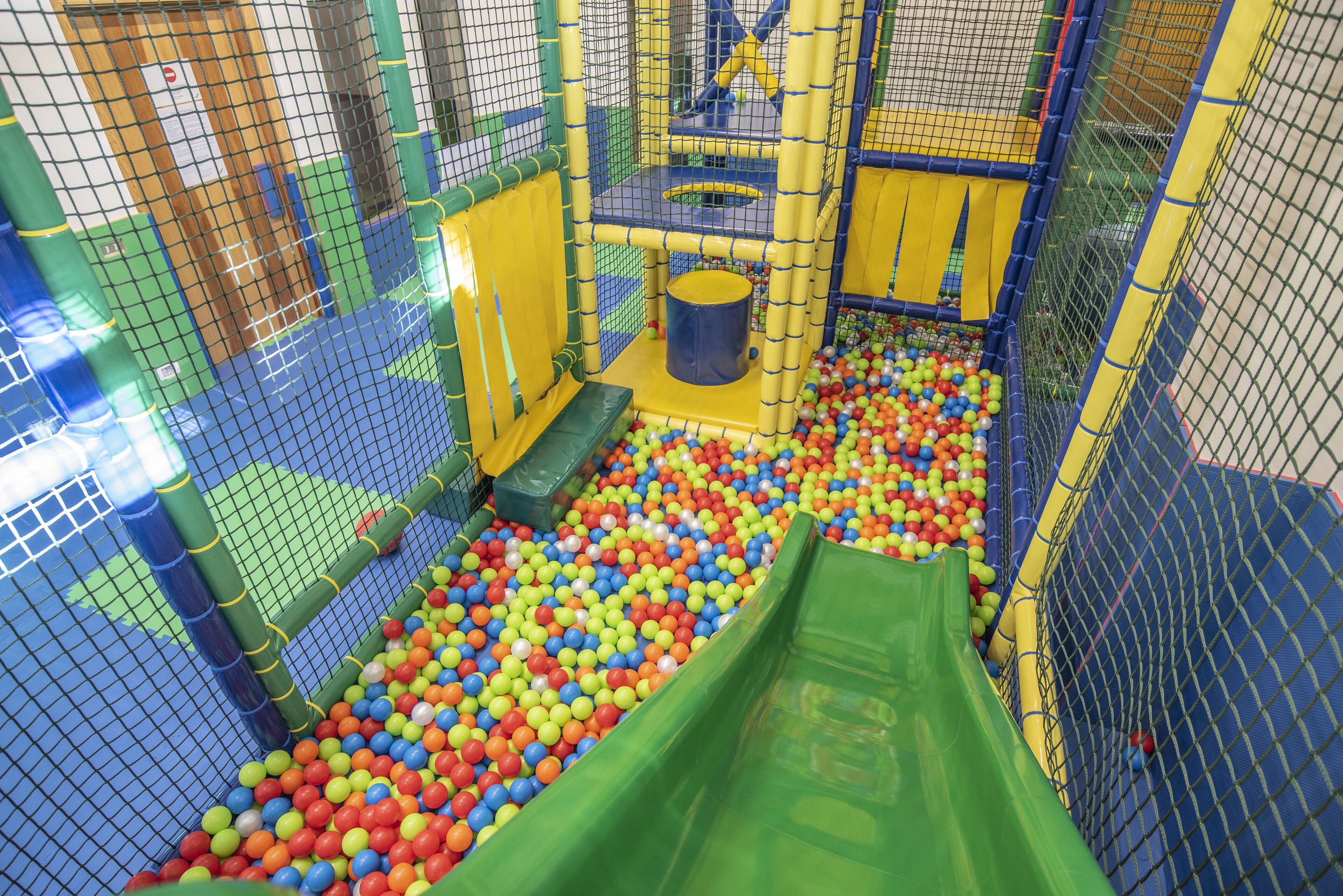 Zona de juegos con piscina de pelotas, tobogán y estructura para escalar.