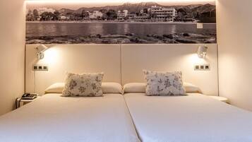Camera d'albergo con un letto grande, due cuscini, lampade ai comodini, un comodino con un telefono e un quadro appeso al muro raffigurante un paesaggio costiero.