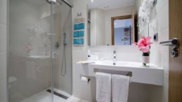 A modern bathroom with a glass shower enclosure, a white sink, and a mirror above it.