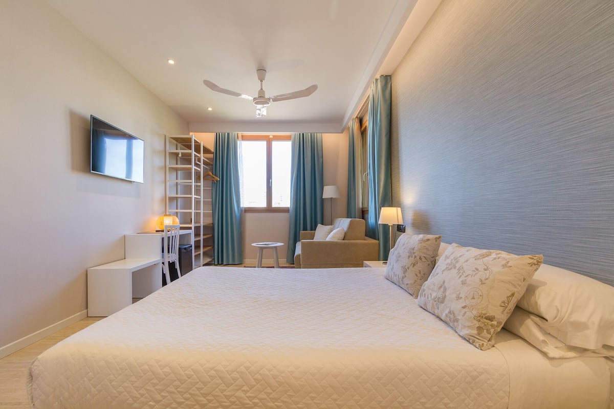 Habitación de hotel con una cama grande, un escritorio, una silla, un armario y un ventilador de techo.