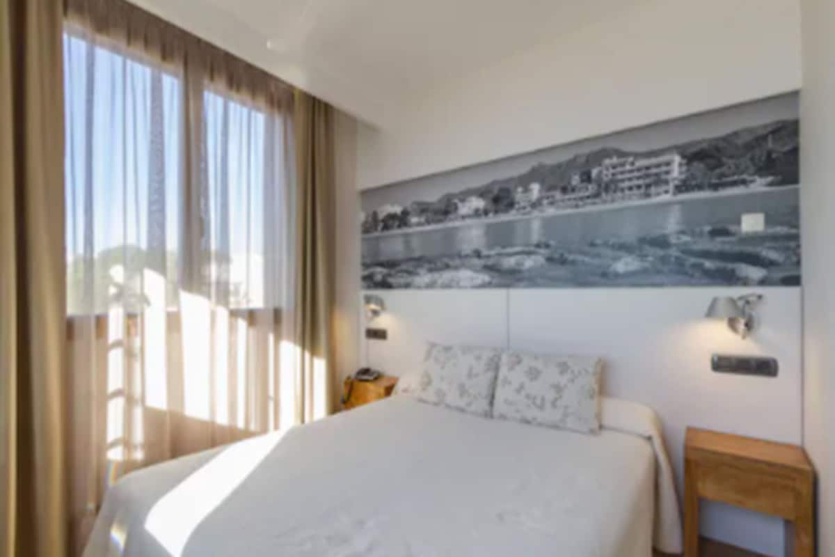 Habitación de hotel con una cama grande, vista a un cuerpo de agua y un cuadro de un paisaje urbano en la pared.