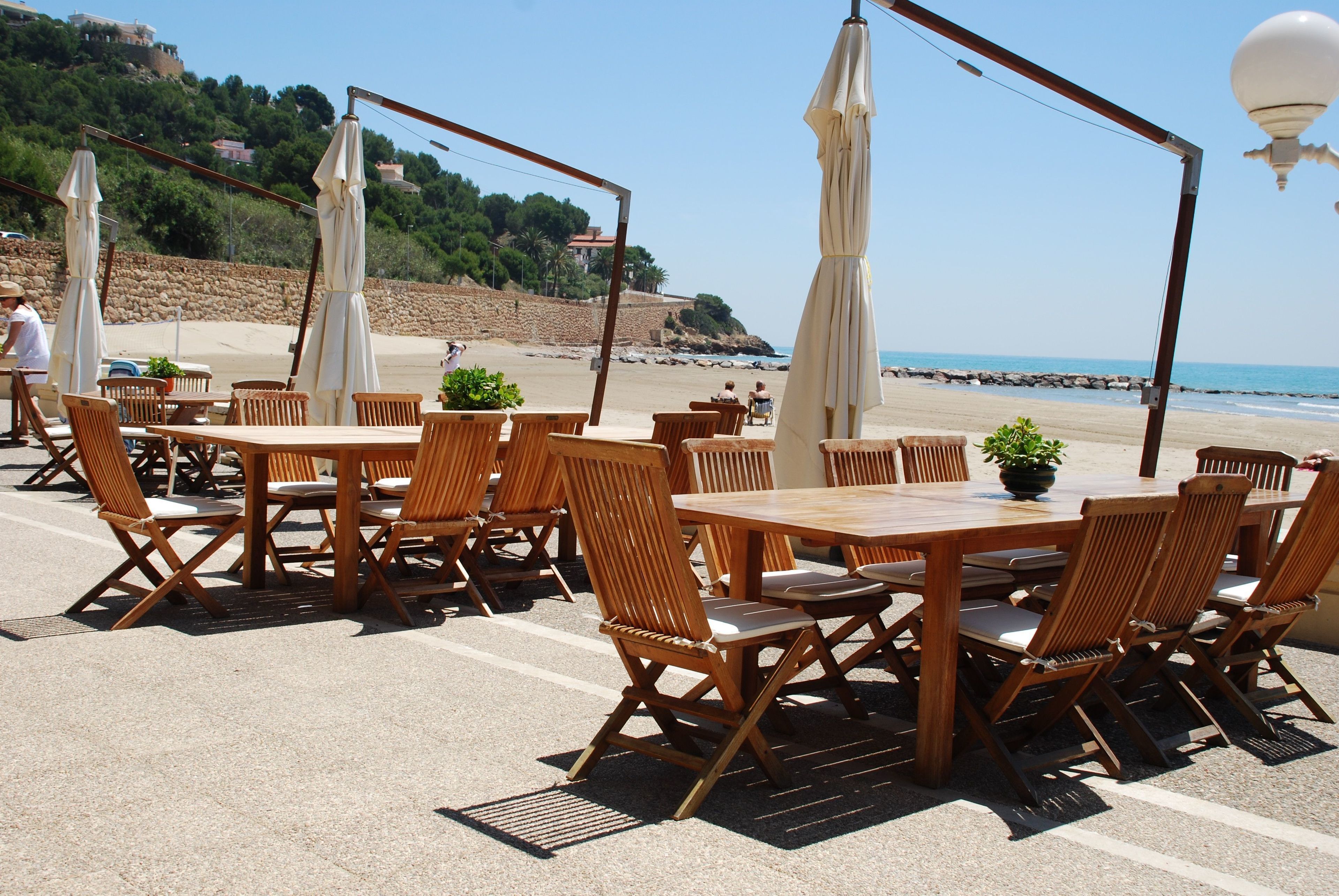 An outdoor seating area with wooden tables and chairs, umbrellas, and potted plants.