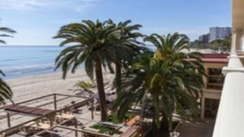 Blick vom Balkon auf einen Strand mit Palmen und einem wolkenlosen Himmel.