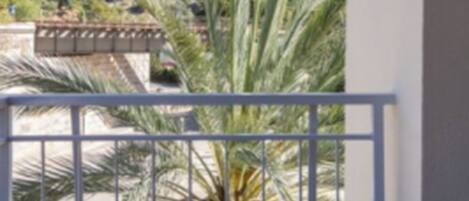 A balcony with a view of a hillside, a palm tree, and a railing.