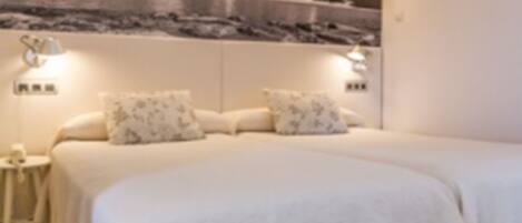 A bedroom with two beds, a nightstand, and a wall-mounted shelf.