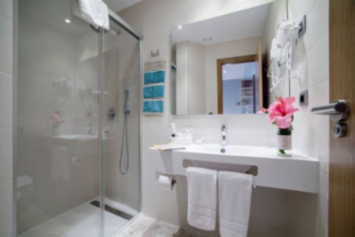 Un baño moderno con cabina de ducha de vidrio, un lavabo blanco con espejo y un perchero para toallas.
