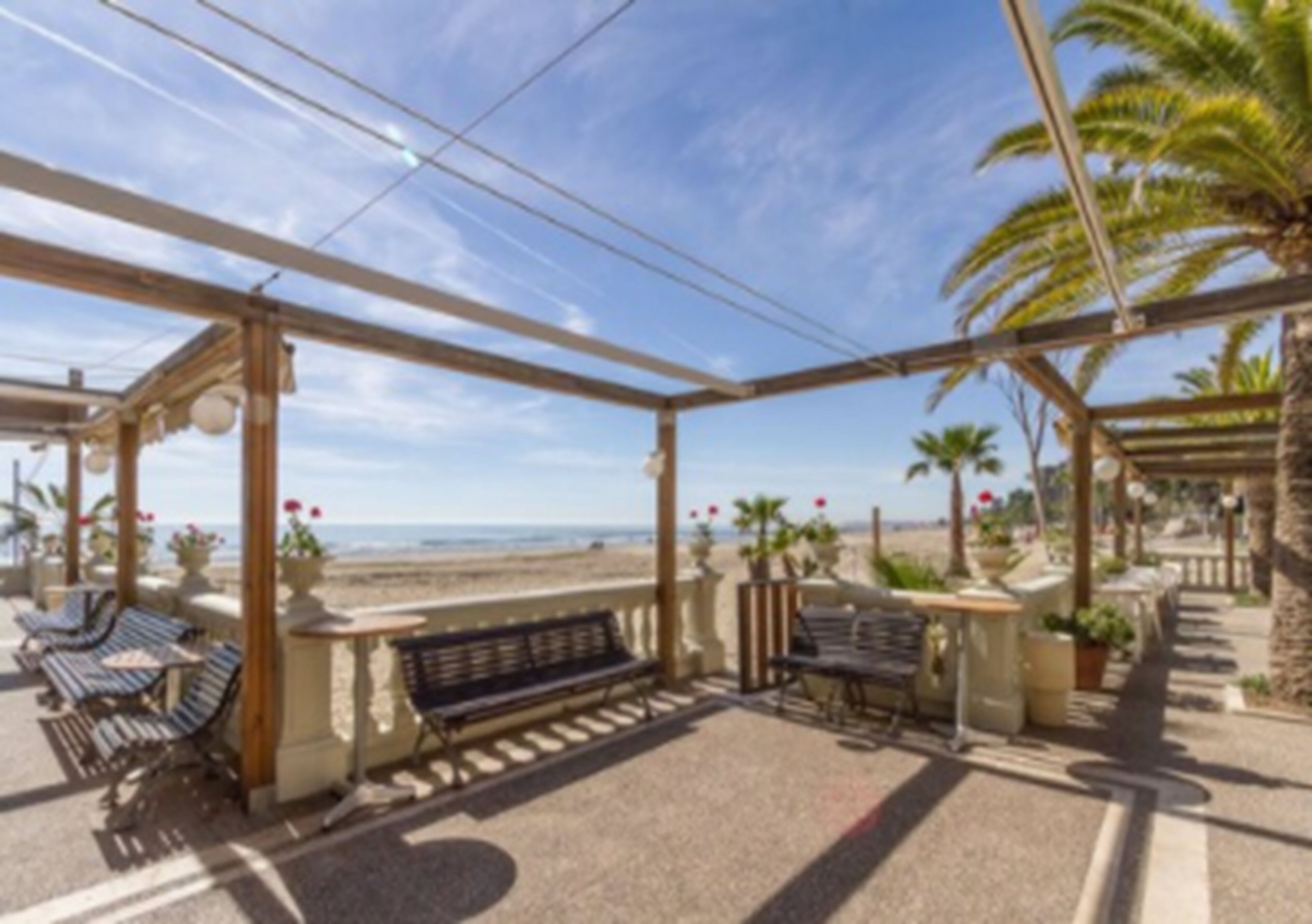 Un espacio de estar al aire libre cubierto con bancos y mesas, con vista a la playa.