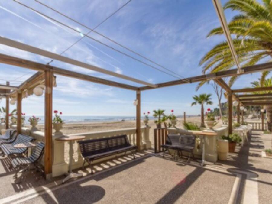 Un espacio de estar al aire libre cubierto con bancos y mesas, con vista a la playa.