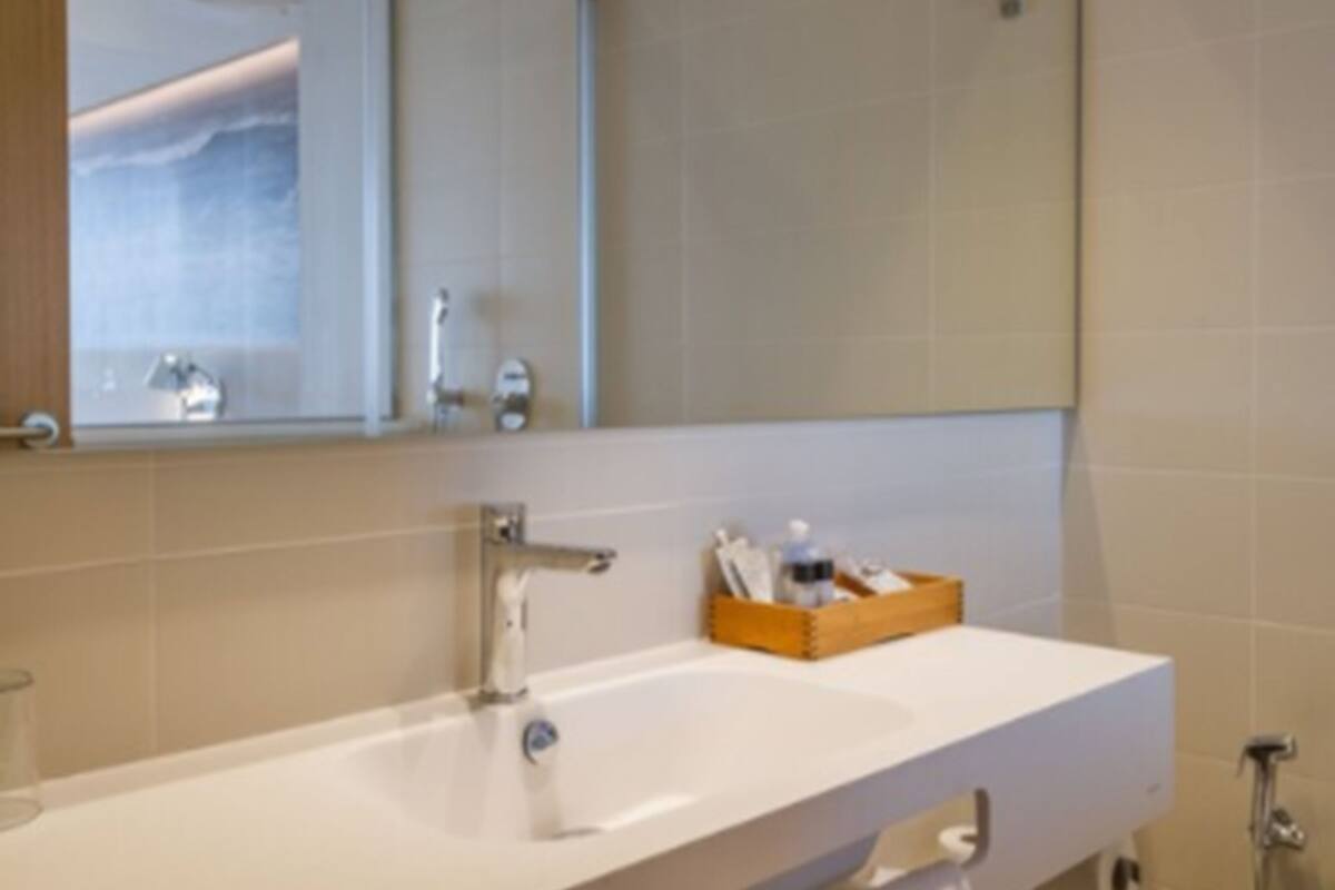 Un baño con un lavabo blanco, un espejo y una caja de madera con artículos de aseo.