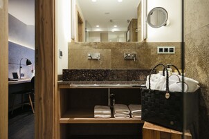 Une salle de bain avec un comptoir en marbre, un miroir, un porte-serviettes et un sac noir tissé.