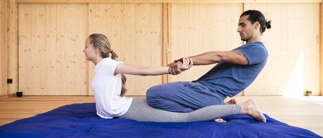 Two people practicing yoga on a blue mat in a room with wooden walls.