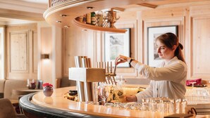 A bar area with a bartender pouring a drink, a bar counter, and a seating area with chairs. - Staudacherhof (Garmisch-Partenkirchen)