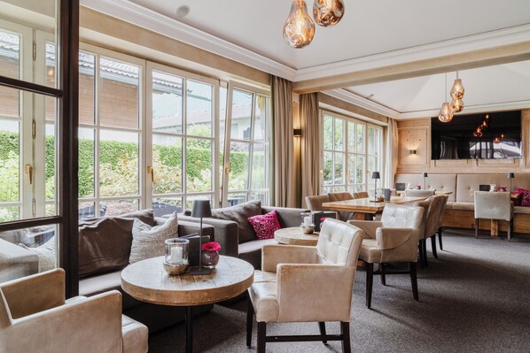 A spacious room with large windows, a sofa, a round coffee table, and a dining area with chairs and a table. - Staudacherhof (Garmisch-Partenkirchen)