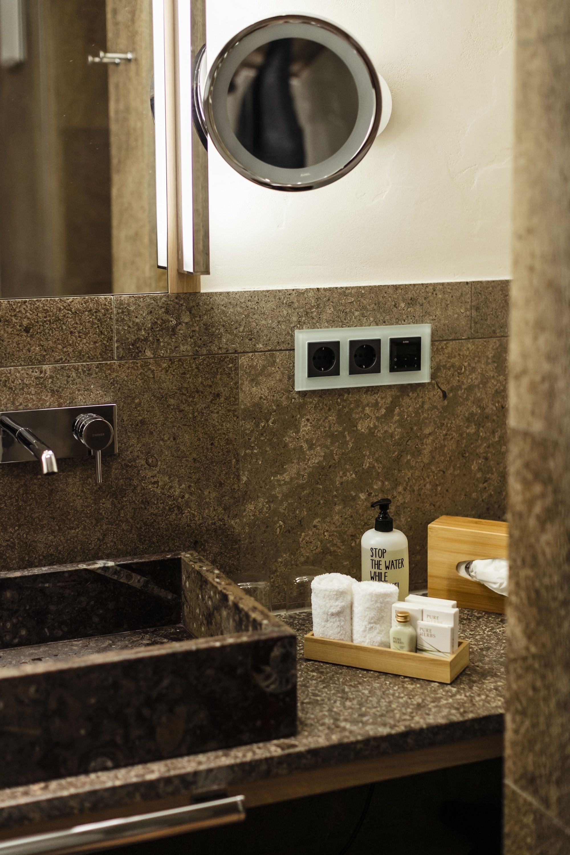 A bathroom with a marble sink, a mirror, a towel rack, and a soap dispenser.