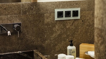 A bathroom with a marble sink, a mirror, a towel rack, and a soap dispenser.