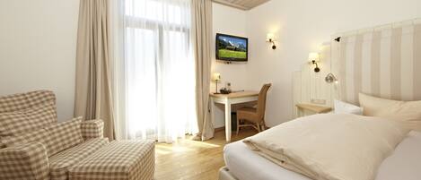 A hotel room with a bed, a desk, a chair, and a television.