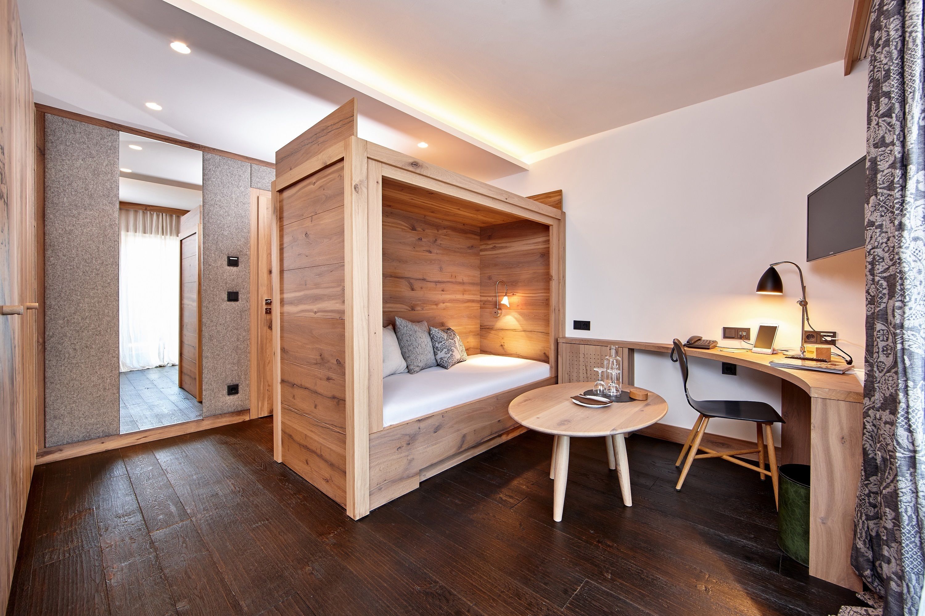 A compact room with a wooden bed, a small table, and a desk with a chair.