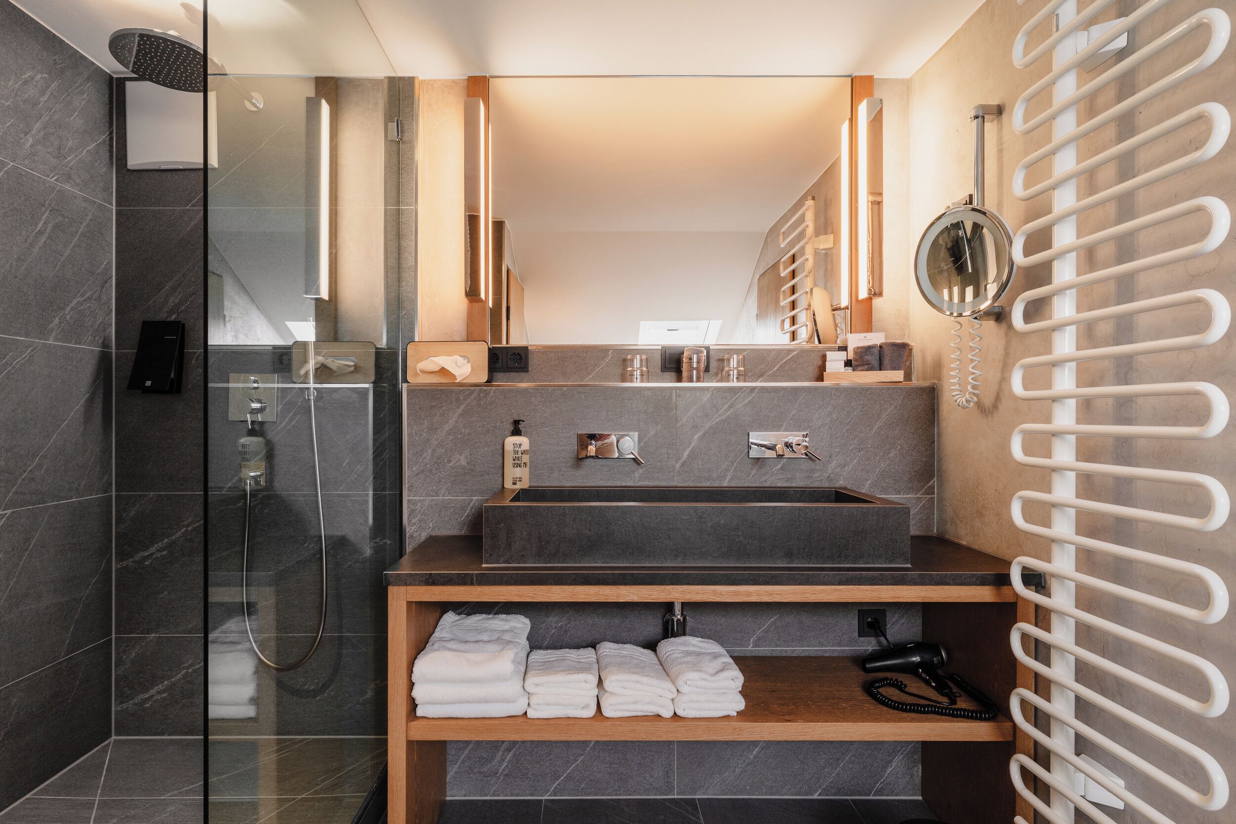 Un bagno moderno con box doccia in vetro, lavabo incassato e mobile bagno in legno con asciugamani.