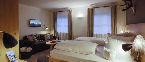 Ein Hotelzimmer mit Bett, Schreibtisch, Stuhl, Sofa, Fernseher und einem an der Wand befestigten Hirschkopf.