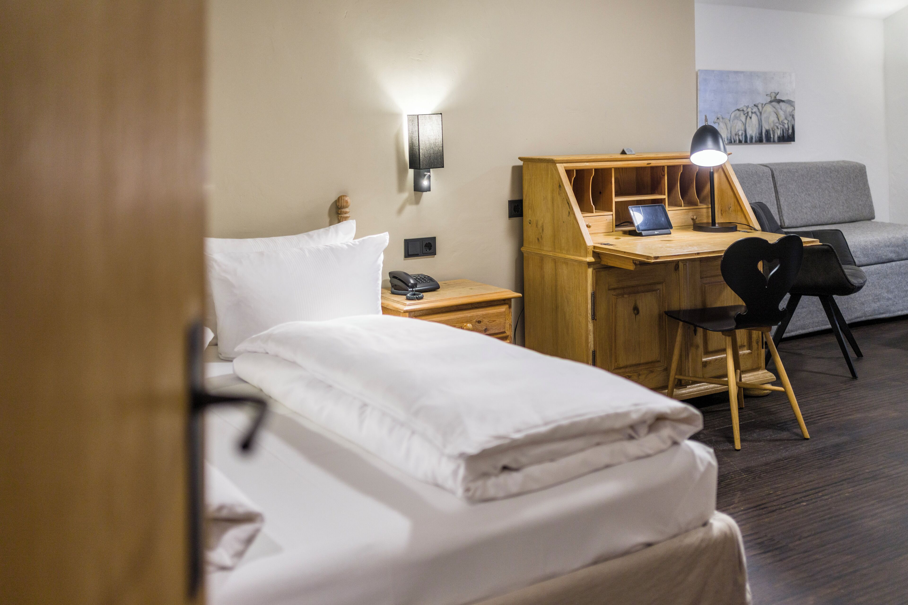 A hotel room with a bed, a desk with a laptop, a chair, a lamp, and a sofa.