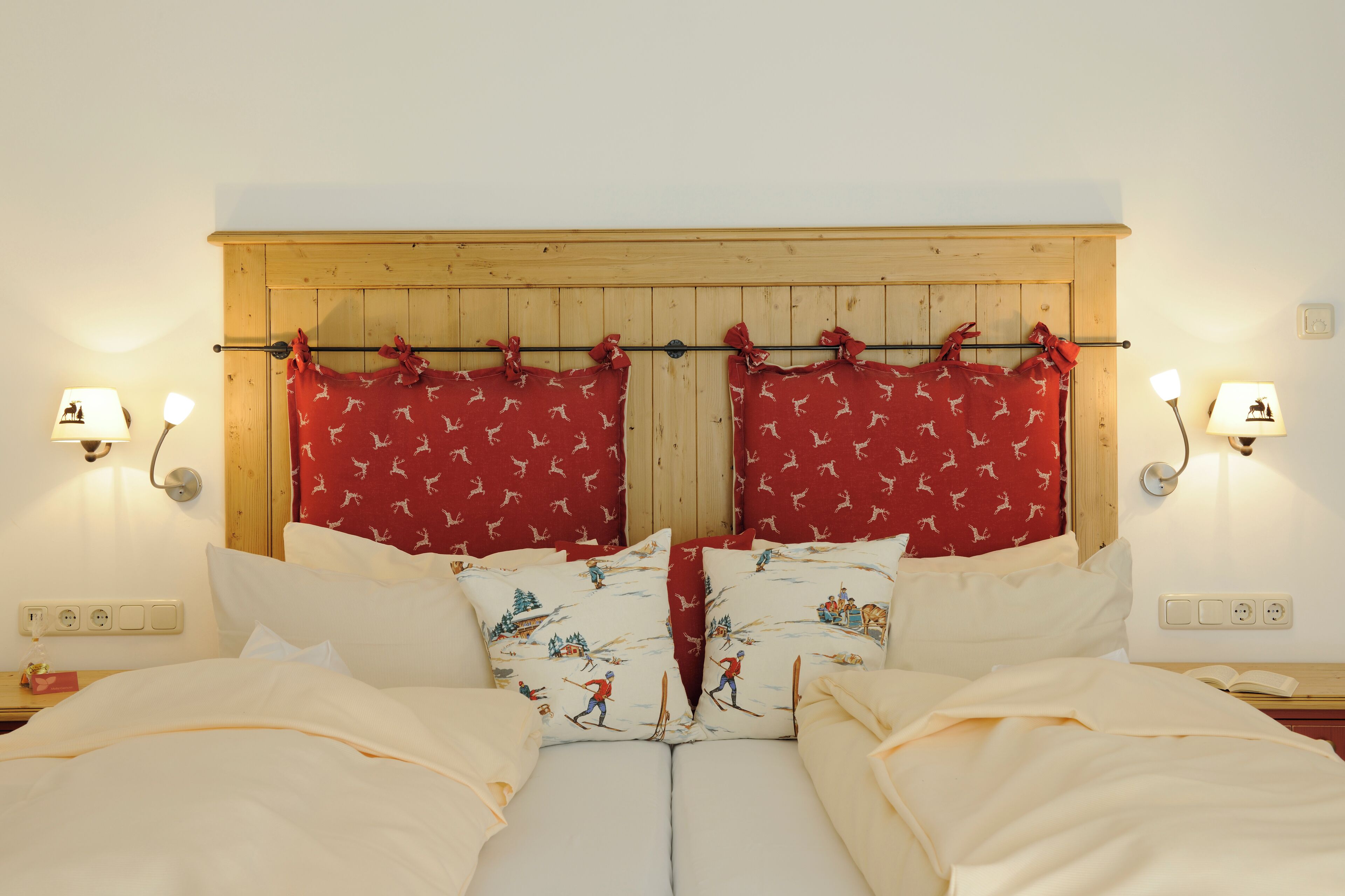 A double bed with white bedding and red curtains with a ski pattern.