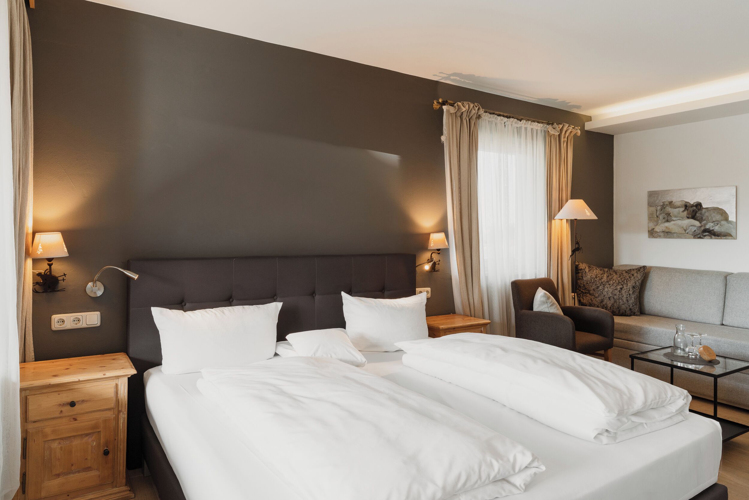 Quarto de hotel com uma cama grande, duas mesas de cabeceira, uma cadeira, um sofá e uma pequena mesa com abajur.