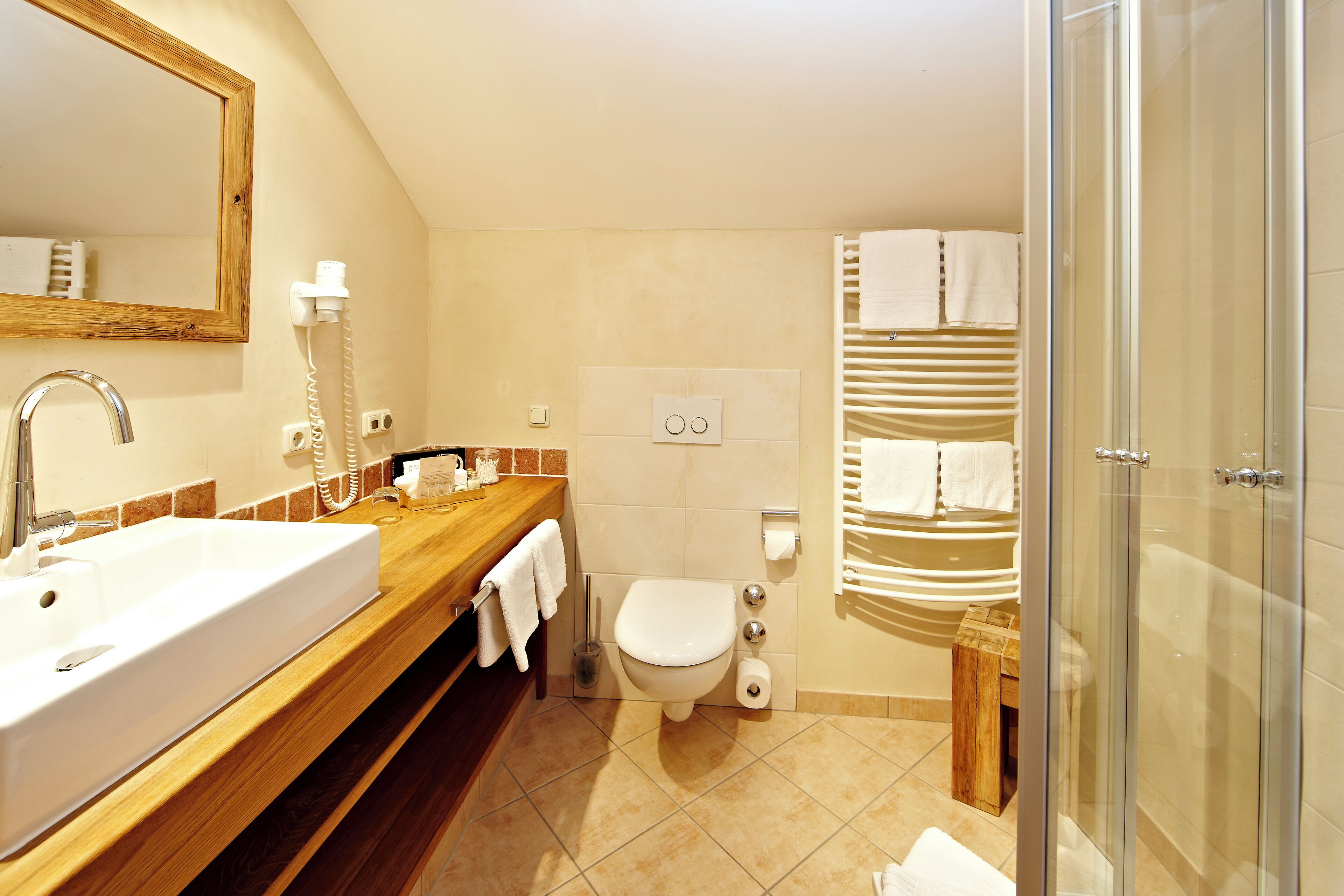 A bathroom with a wooden vanity, a large mirror, a white sink, a toilet, and a glass shower enclosure.