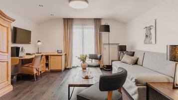 A modern hotel room with a wooden desk, a sofa, a TV, and a large window with curtains.