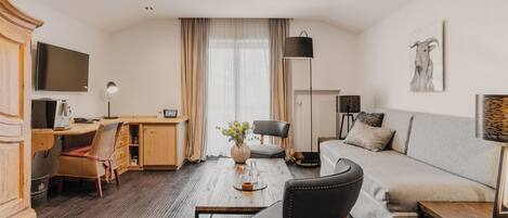 Une chambre d’hôtel moderne avec un bureau en bois, un canapé, une télévision et une grande fenêtre avec des rideaux.