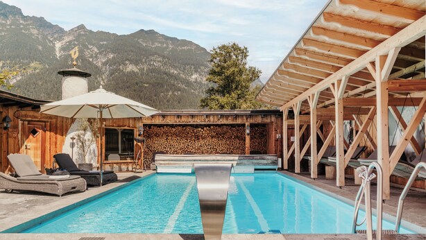 A wooden pool area with lounge chairs, a wooden deck, and a mountain backdrop. - Staudacherhof (Garmisch-Partenkirchen)