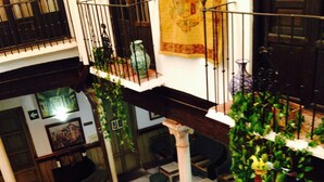 A spacious indoor area with multiple seating arrangements, including wicker chairs and tables, and a balcony with a railing. - Casa Palacio Pilar del Toro (Granada)