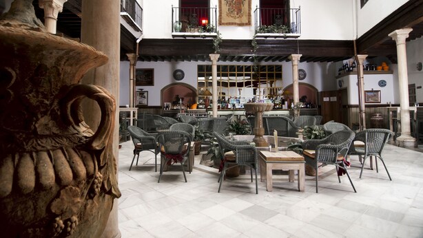 A spacious courtyard with wicker furniture, a fountain, and a large column. - Casa Palacio Pilar del Toro (Granada)