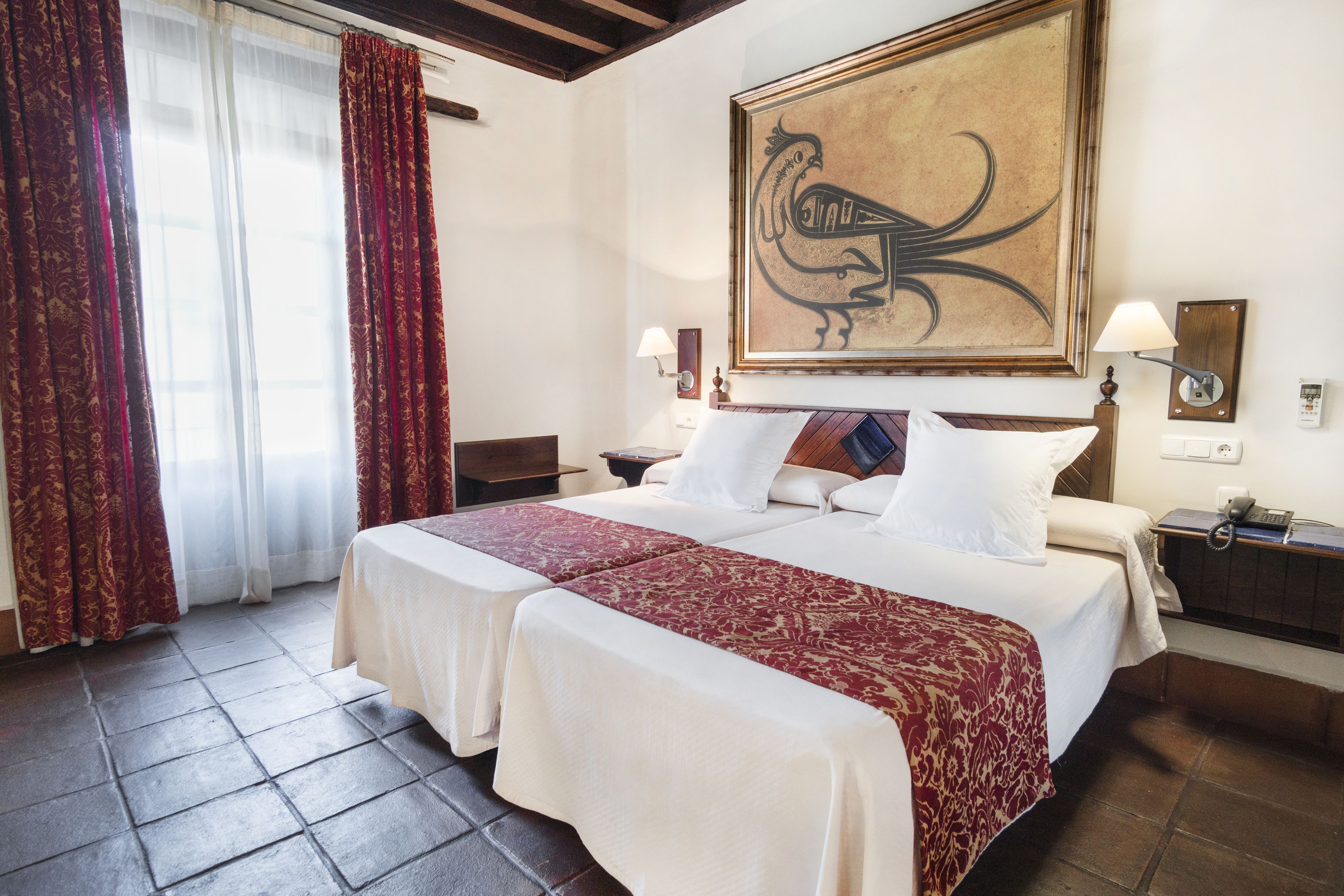 Une chambre d’hôtel avec deux lits, un grand tableau au mur, une lampe sur la table de chevet et un téléphone sur la table d’appoint.