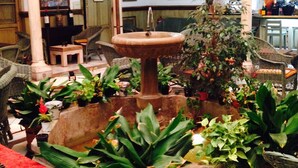 A traditional interior with a central fountain, surrounded by potted plants and wicker furniture. - Casa Palacio Pilar del Toro (Granada)