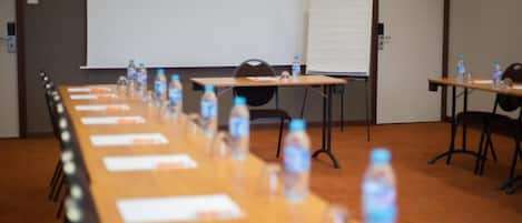 Un salón de conferencias con una larga mesa, sillas, botellas de agua y una pizarra.