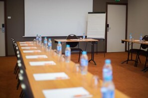 Een vergaderzaal met een lange tafel, stoelen, waterflesjes en een whiteboard.